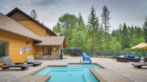 Un área de piscina con sillones de descanso, un espacio de estar techado y una cabaña de madera.