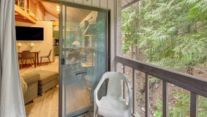 Una habitación con puerta de vidrio corredera, un sofá, una silla, un televisor y vistas a árboles fuera.