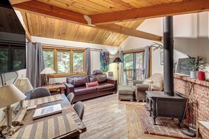 A cozy living room with a fireplace, wooden ceiling beams, and large windows. - Whitefish Lake Couples Escape w/ Community Perks! (Whitefish)