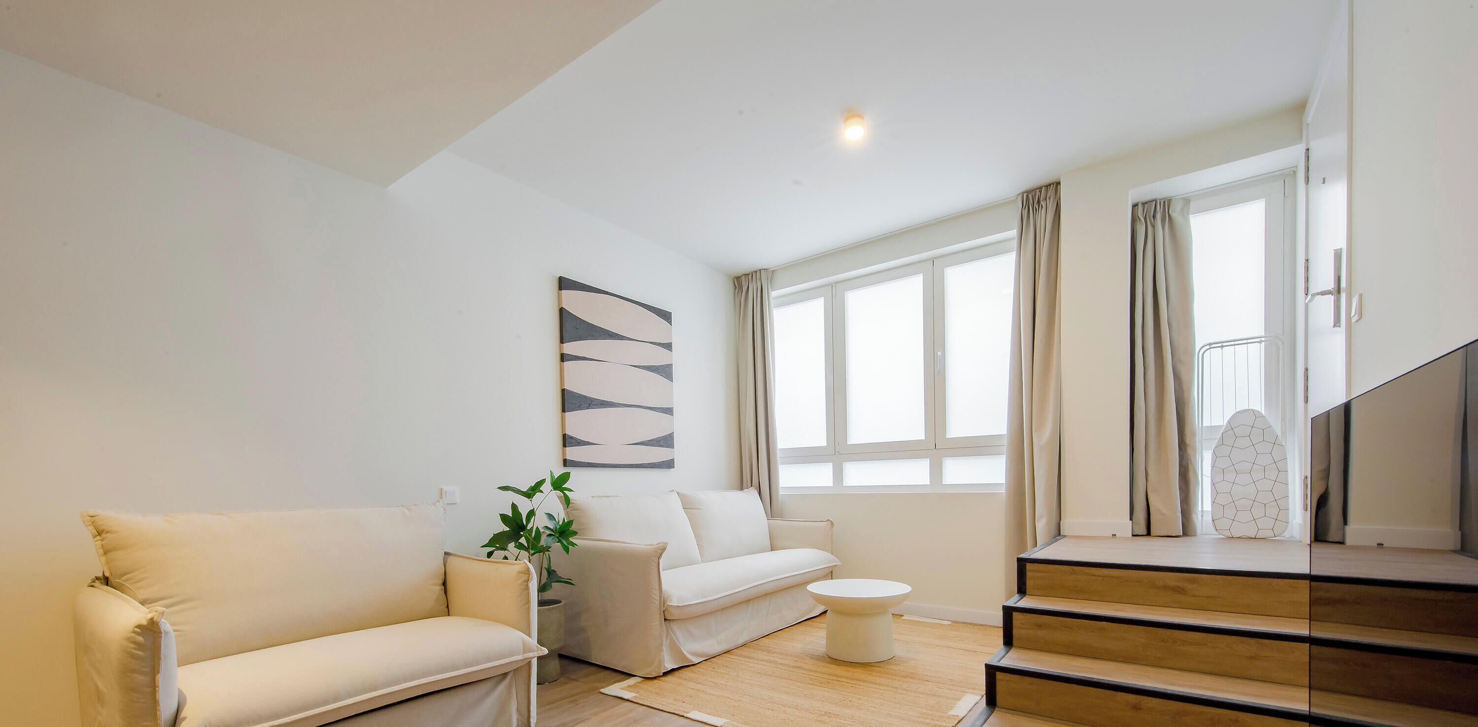 A modern living room with a sofa, a coffee table, a potted plant, and a staircase.