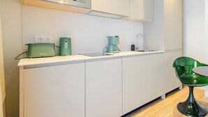 Une cuisine moderne avec des meubles blancs, un four à micro-ondes, une machine à café et une chaise verte.