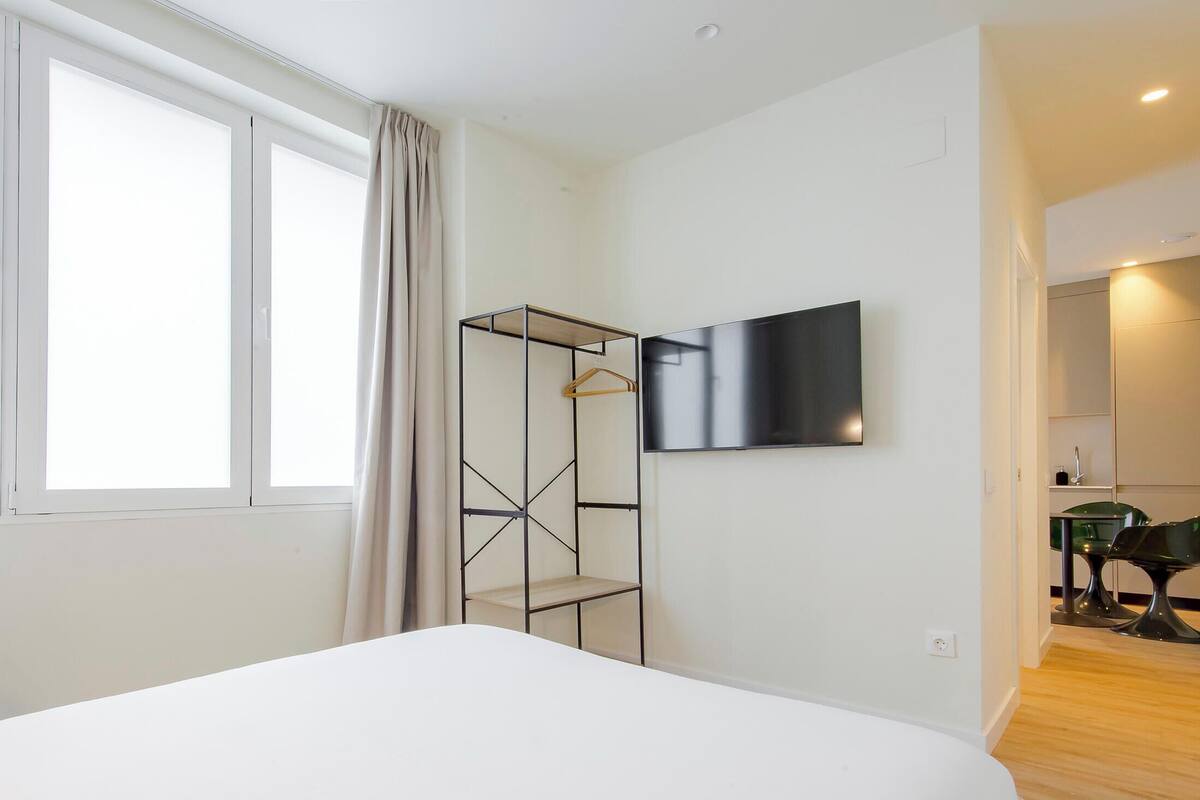 Una habitación de hotel moderna con una cama grande, un televisor montado en la pared, un vestidor amplio y una pequeña zona de comedor.