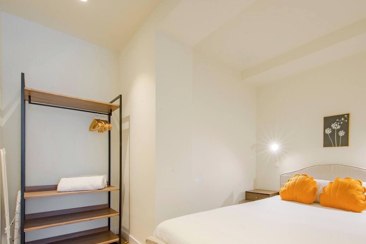 Un dormitorio con cama, mesita de noche, estante en la pared y lámpara de pared.