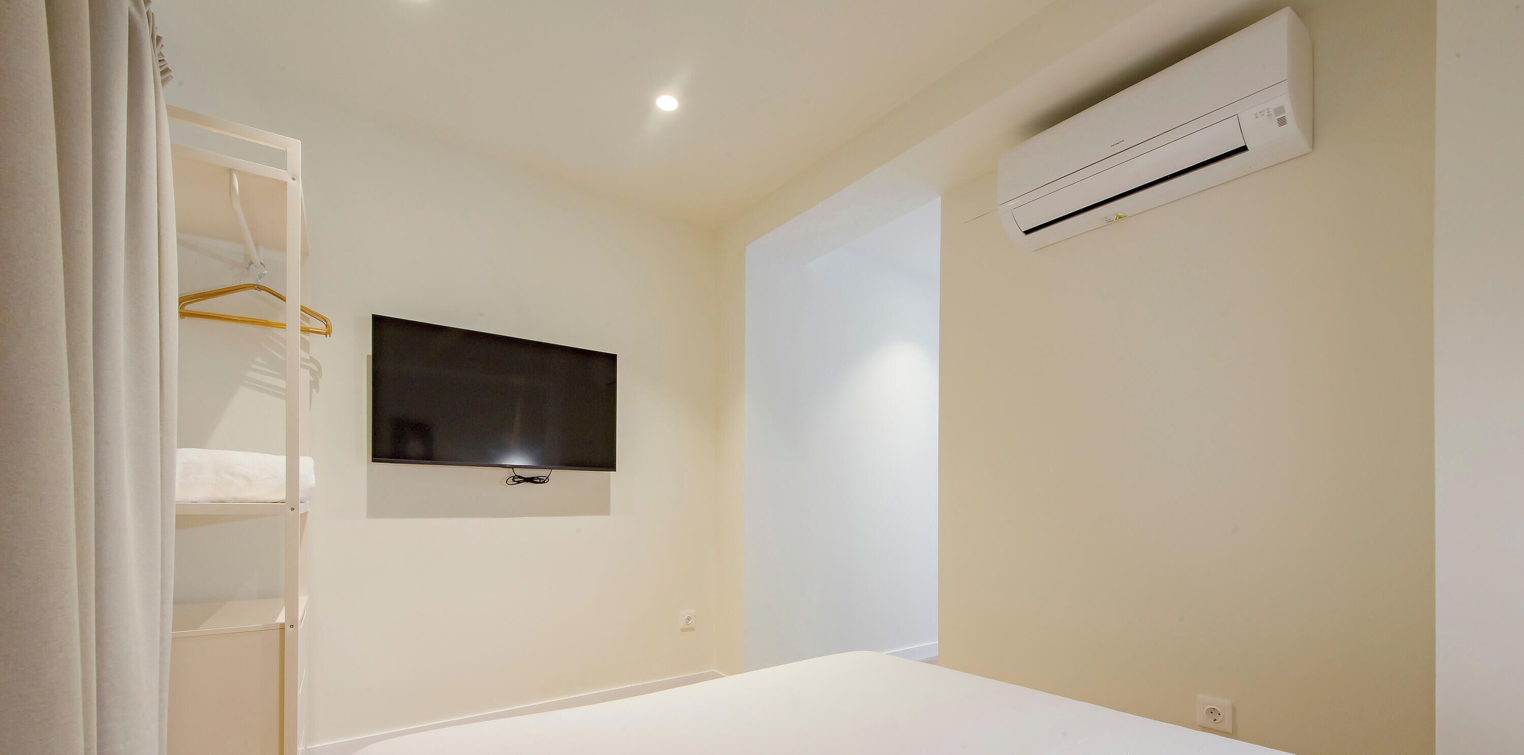A bedroom with a bed, a TV mounted on the wall, and an air conditioning unit.