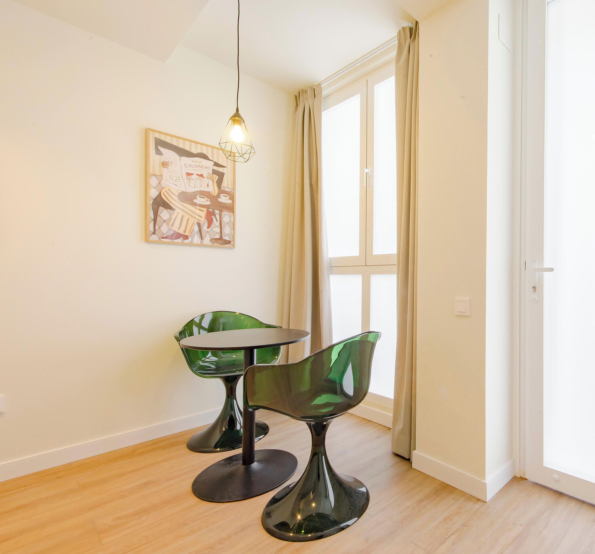 A room with a dining table, two green chairs, a hanging light fixture, and a window with curtains.