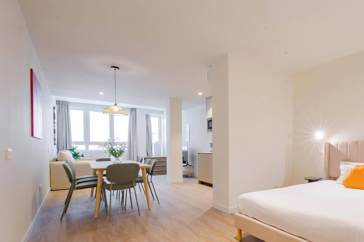 Una habitación de hotel moderna con una cama, mesita de noche y un comedor con sillas y una mesa.