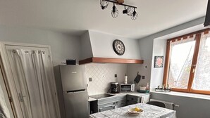 Kompakti keittiö, jossa on jääkaappi, mikroaaltouuni ja liesi, ruokapöytä tuoleineen sekä ikkuna, josta on näkymä.