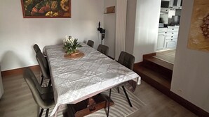 Ruokailutila, jossa on pöytä, tuoleja ja seinällä taulu.
