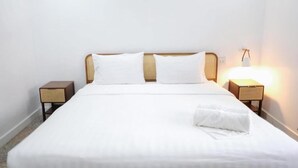 Een opgemaakt bed met witte lakens, twee nachtkastjes met gevlochten manden en een wandlamp.