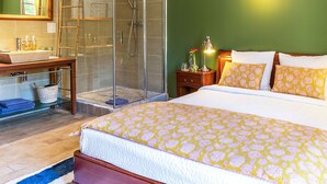 Une chambre à coucher comprenant un lit, une table de chevet, une commode, un miroir, une douche et une salle de bain avec un lavabo et un porte-serviettes.