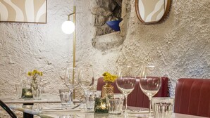 Un espace repas agrémenté d’un mur en pierre, d’une table en marbre, de sièges en cuir rouge et d’un miroir décoratif.