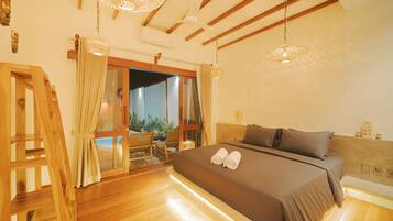 A bedroom with a large bed, wooden floor, ceiling fan, and a view of the outdoors.
