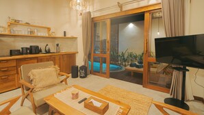 Una sala de estar acogedora con una mesa de centro de madera, un sillón cómodo, un televisor de pantalla plana y un ventanal corredero que da a una zona de piscina.