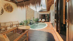 Una terraza de madera con piscina, mobiliario de mimbre y techo de paja.