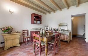 A dining area with a wooden table, chairs, a cabinet, and a kitchen area with a microwave and stove. - Preseglie Lake Garda - Rosa Canina (Desenzano Del Garda)
