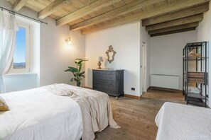 A bedroom with a bed, dresser, lamp, plant, and a view of the outdoors. - Preseglie Lake Garda - Rosa Canina (Desenzano Del Garda)