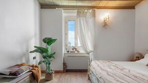 Ein Schlafzimmer mit Bett, Nachttisch, Fenster mit Blick, einer Pflanze und einer Wandleuchte.