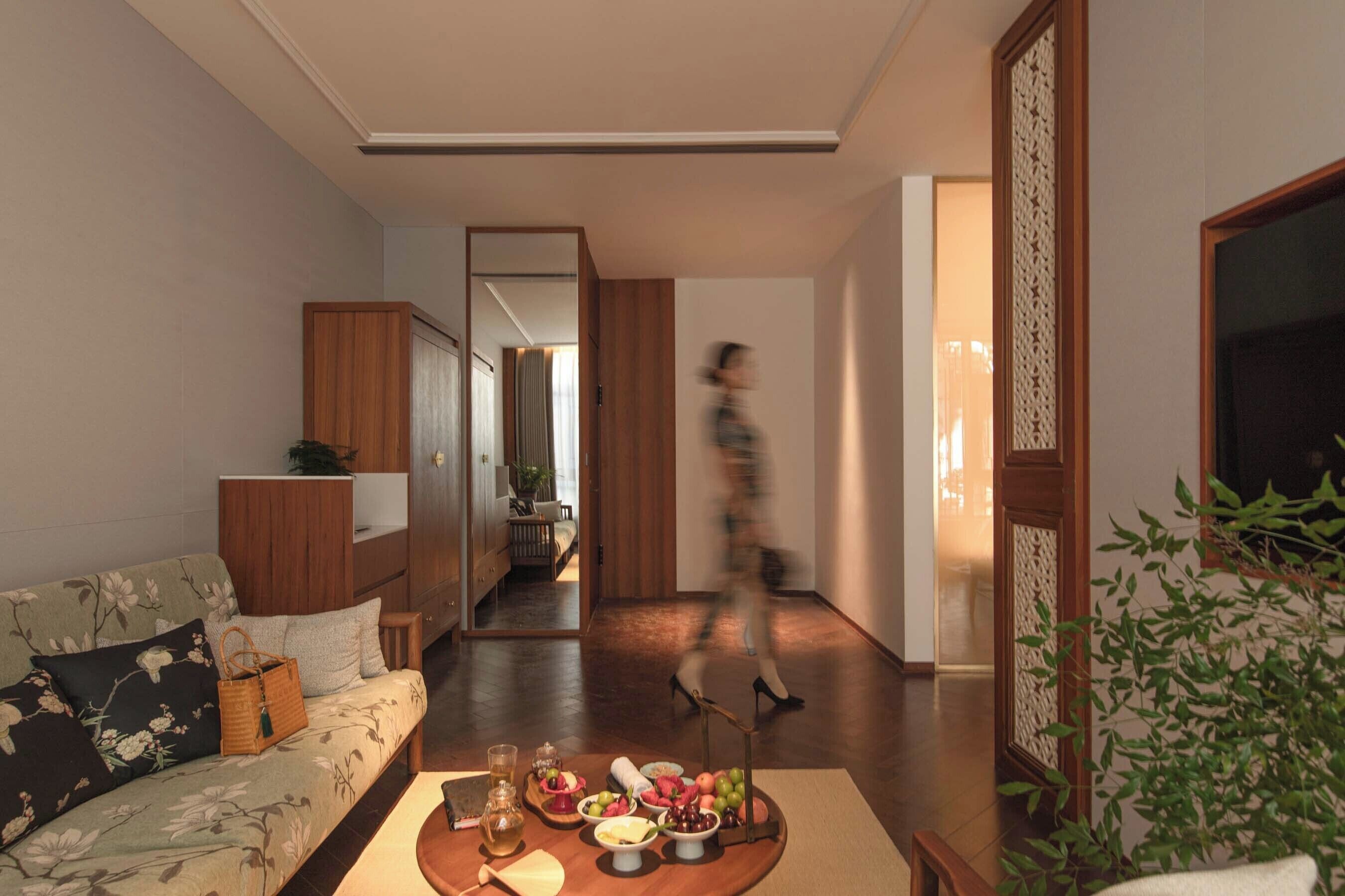 A living room with a sofa, a coffee table with fruits and drinks, a wooden cabinet, and a large mirror.