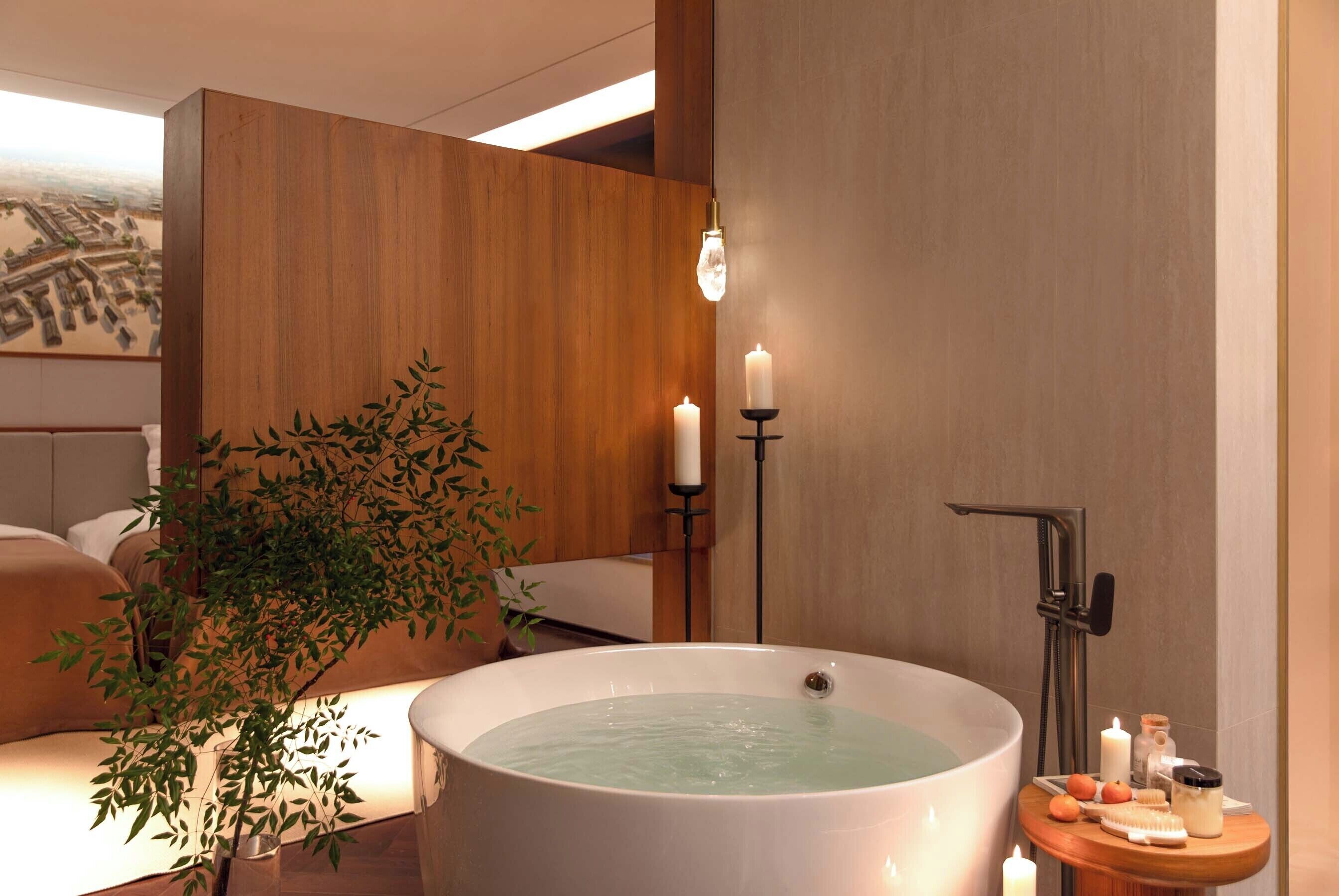A spa room with a large bathtub, a wooden panel wall, a small table with toiletries, and a potted plant.