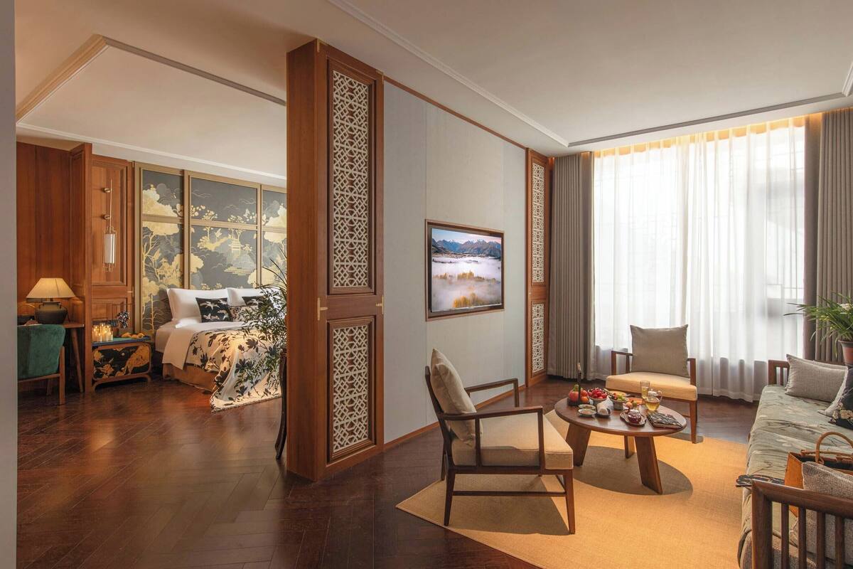 A hotel room with a bed, a sitting area with a coffee table, a TV, and a large window with curtains.
