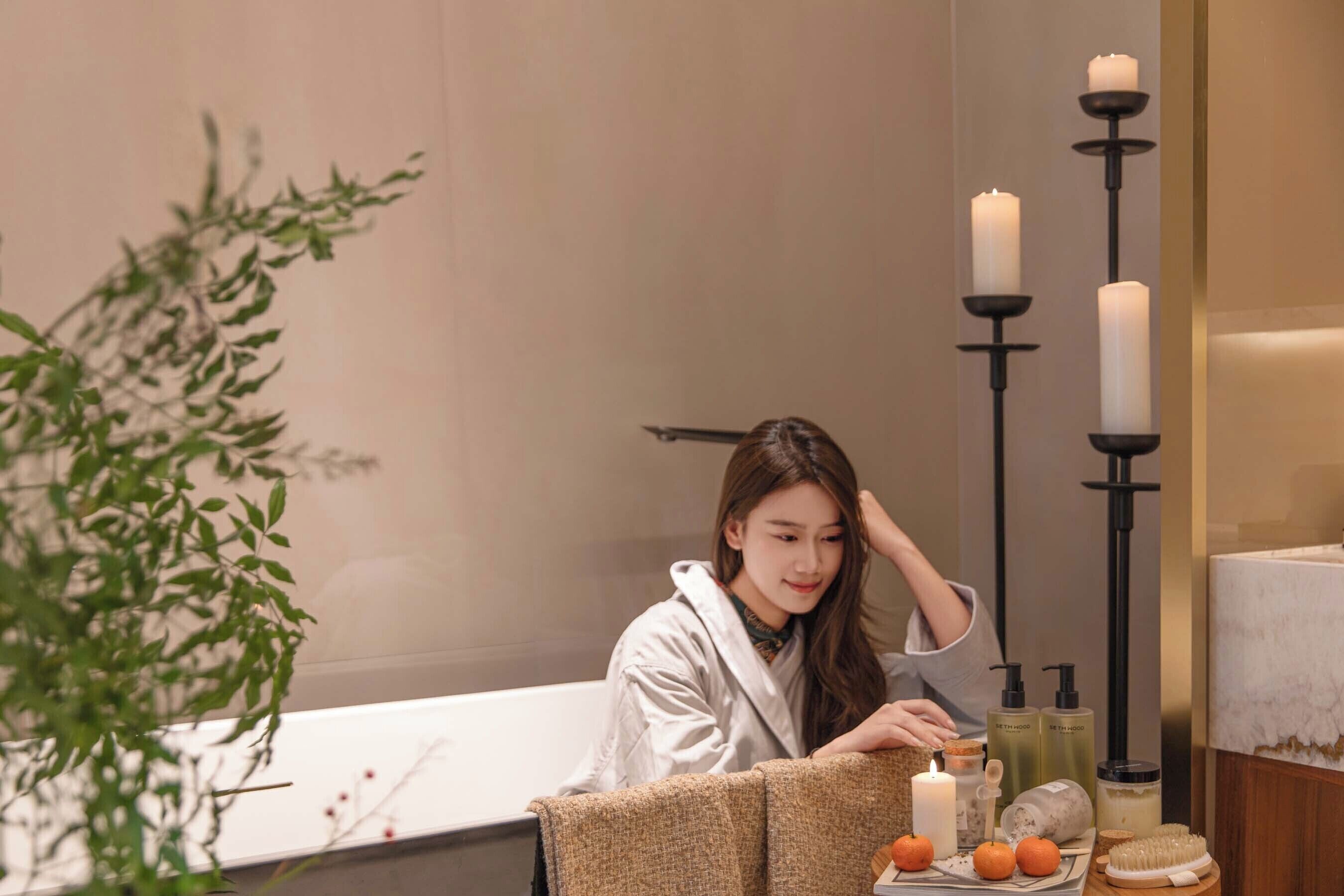 Une salle de bain avec une baignoire, des bougies, des articles de toilette et une plante.