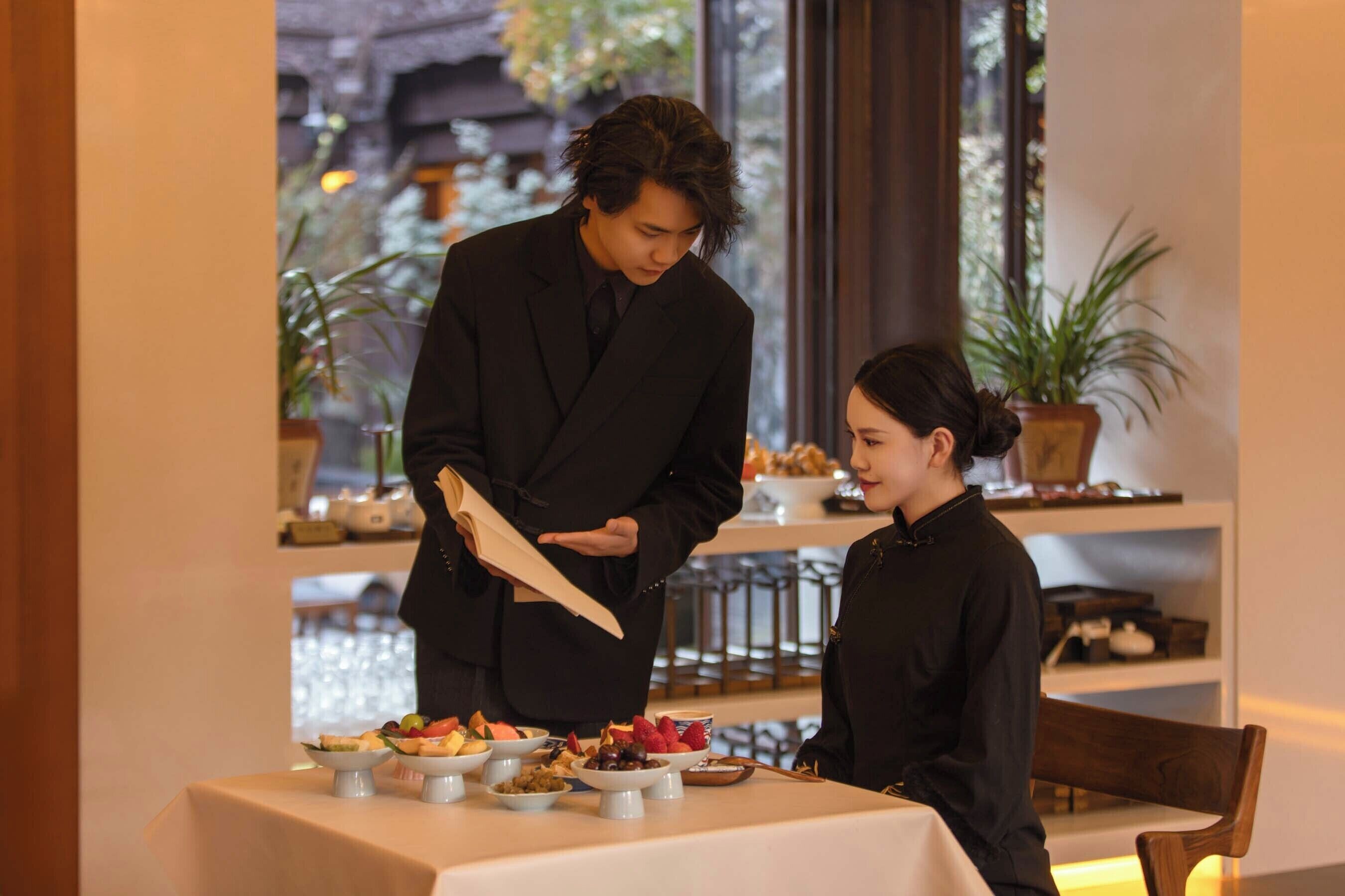 A person serving food to another person at a table with various dishes.