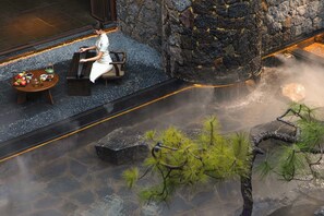 A person playing a piano in a stone-walled room with a table of fruits and a small waterfall feature. - Chinese-style garden resort hotel (Lijiang)
