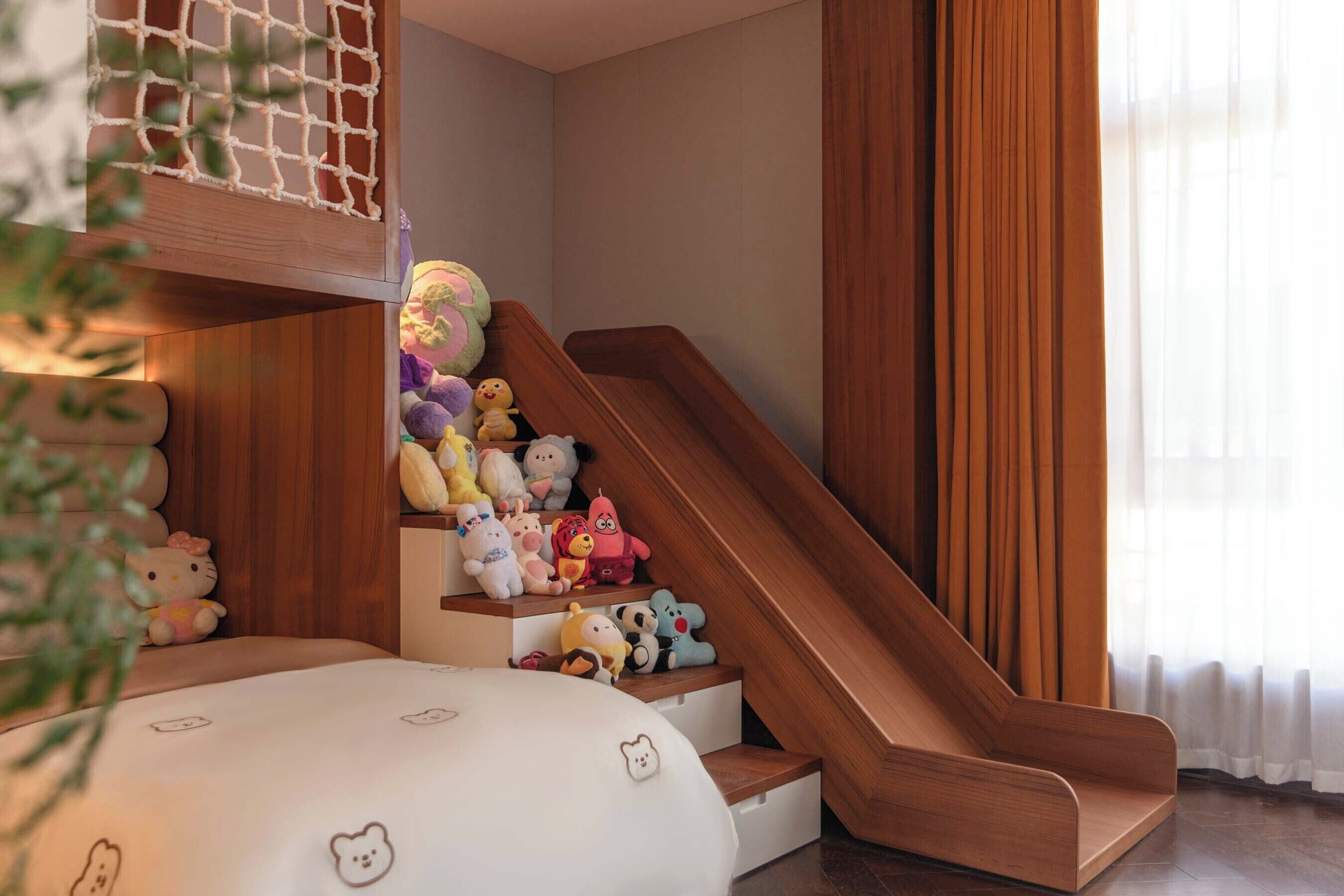 A staircase with a wooden finish, plush toys on the steps, and a white bed with a bear pattern.