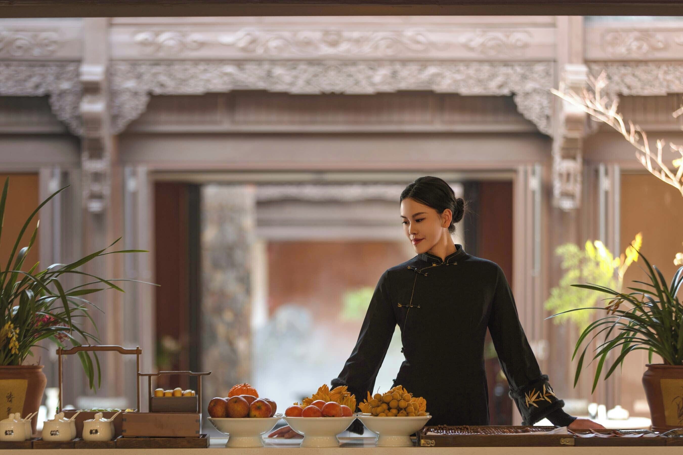 A person in traditional attire serving food at a table with various dishes and a tea set.