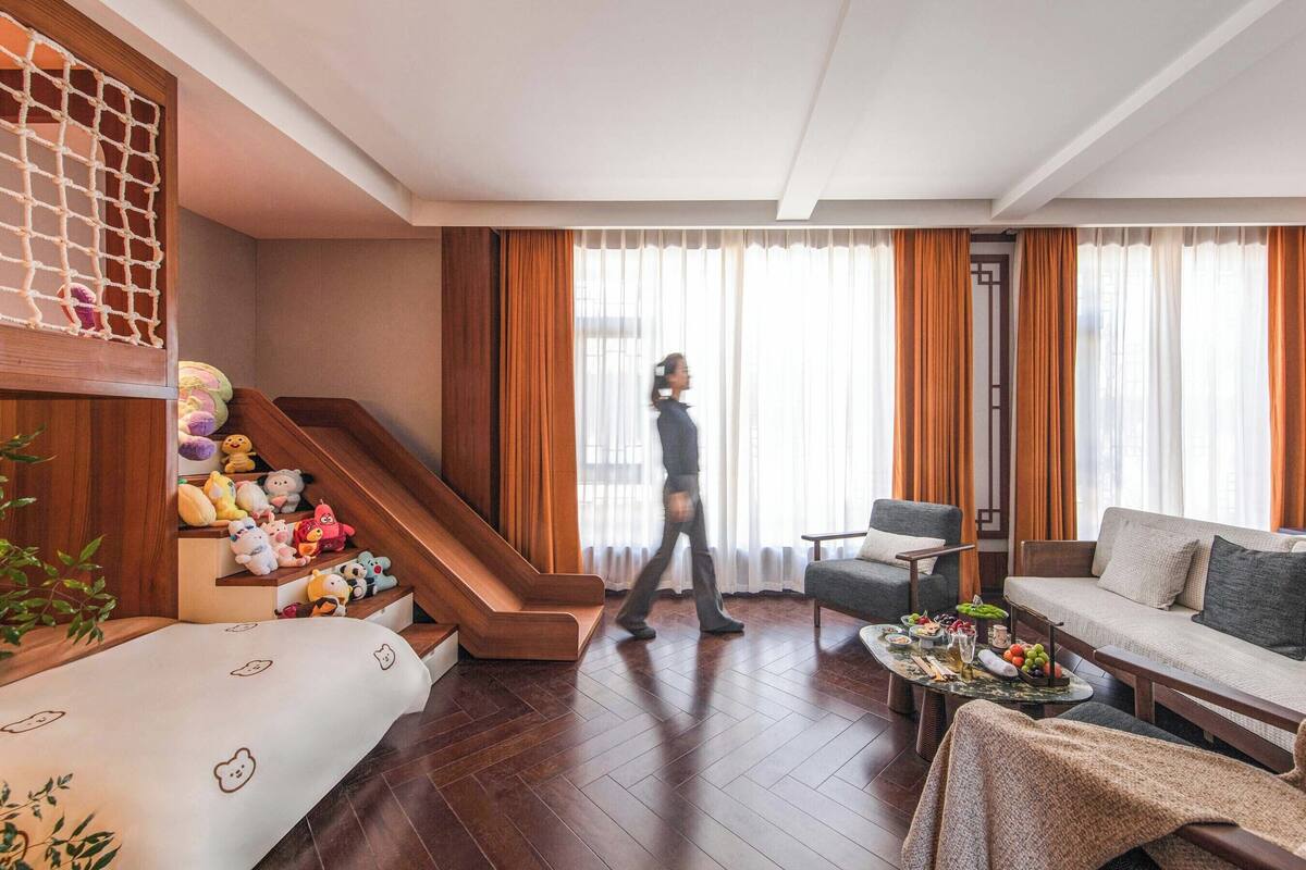 A modern living room with a wooden staircase, a sofa, a coffee table with fruits, and a person walking.