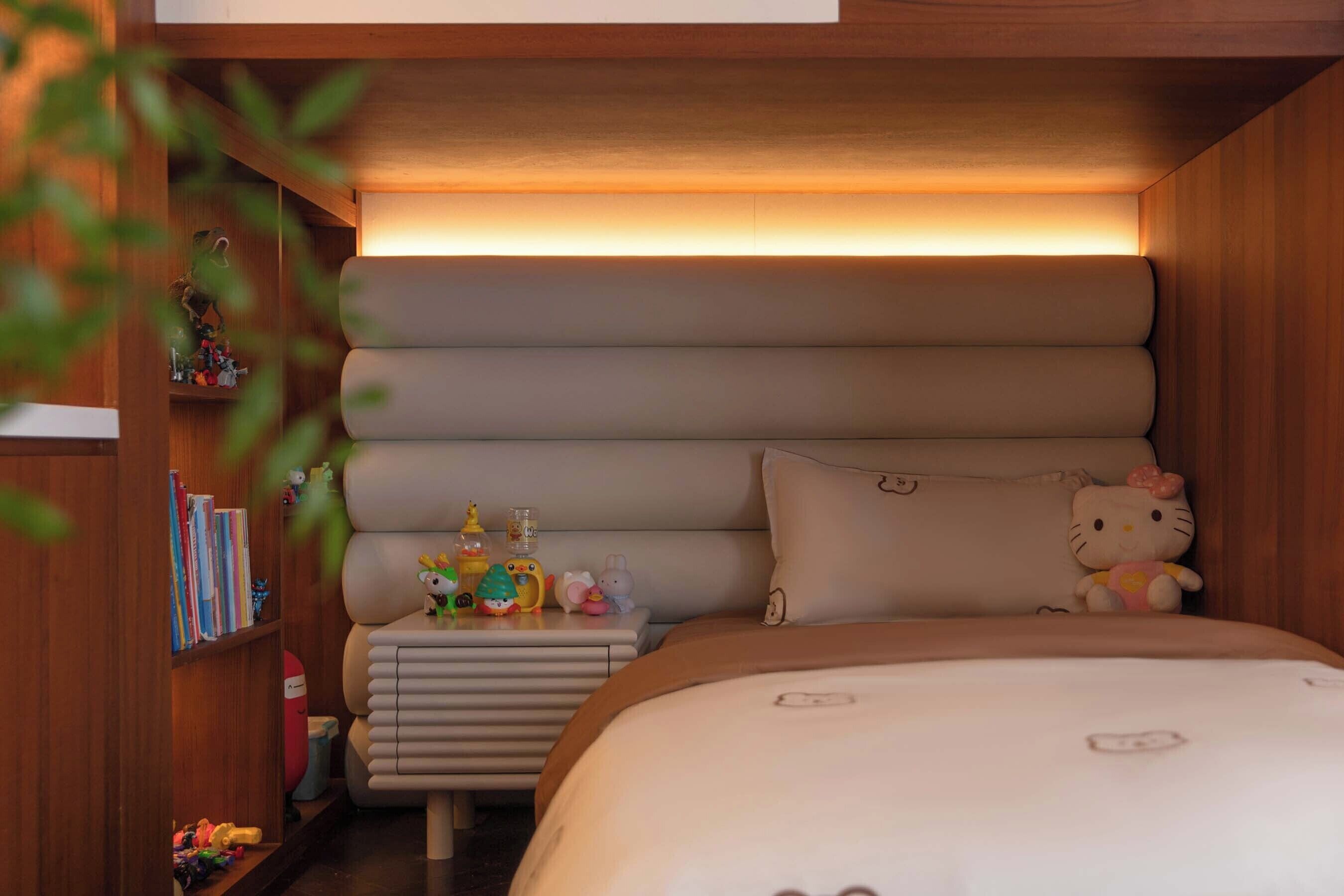 A cozy bedroom with a bed, bedside table, and a shelf with books and toys.