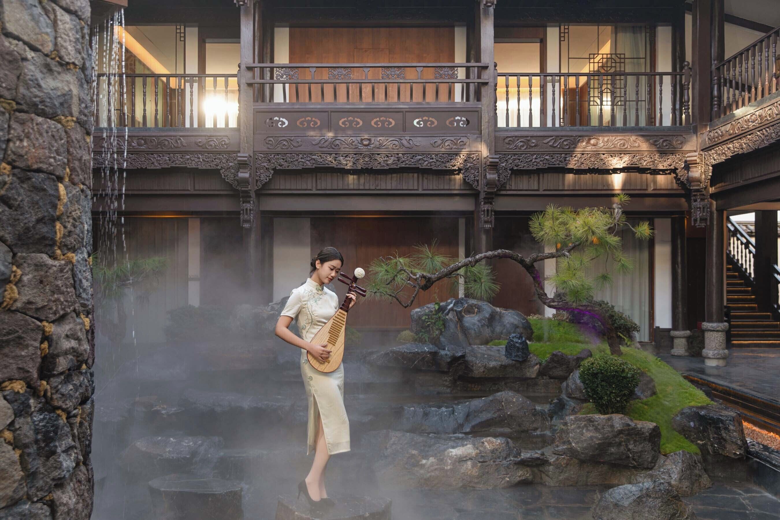 A traditional building with a stone wall, a person playing a stringed instrument, and a rock garden.