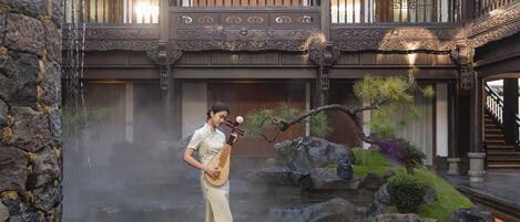 A traditional building with a stone wall, a person playing a stringed instrument, and a rock garden.
