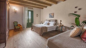 Una habitación con dos camas, piso de madera, una puerta verde y una planta grande.