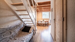A narrow hallway with a staircase, a sofa with a patterned cover, a wooden dining table with chairs, and a window with a view of trees. - Apartment “Côté Soleil” with Mountain View, Balcony and Wi-Fi (Châtel)