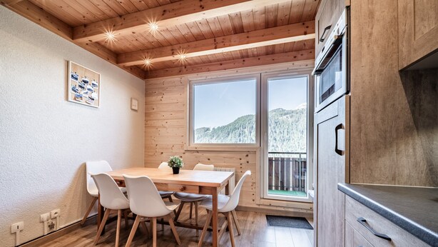A modern kitchen with wooden cabinets, a built-in oven, and a large window offering a view of a forested hill. - Apartment “Côté Soleil” with Mountain View, Balcony and Wi-Fi (Châtel)