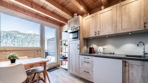 A modern kitchen with wooden cabinets, a built-in oven, and a large window overlooking a forested area. - Apartment “Côté Soleil” with Mountain View, Balcony and Wi-Fi (Châtel)