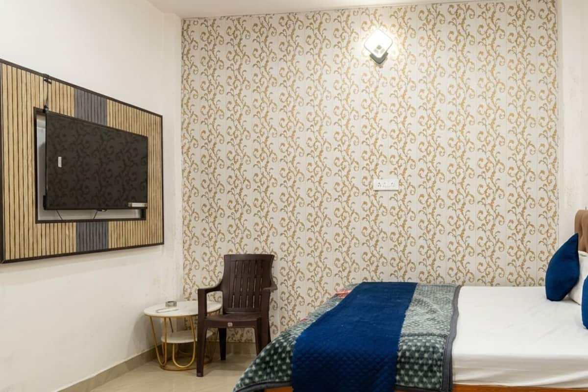 Un dormitori amb un llit, un televisor fixat a la paret, una cadira i una taula petita.