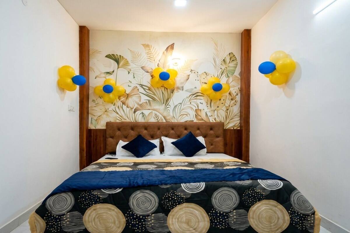 Un dormitori amb un panell de capçal tapissat, un llençol estampat i decoracions florals penjades a la paret.