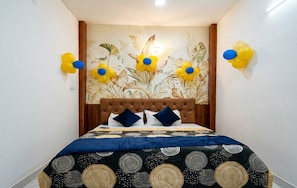 A bedroom with a tufted headboard, a patterned bedspread, and wall-mounted floral decorations. - The Ghat Side home stay (Varanasi)