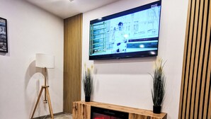 Una sala de estar moderna con un televisor de pantalla plana montado en la pared, un mueble de entretenimiento de madera debajo, una mesa de centro con elementos decorativos y una lámpara de pie.