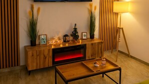 Una sala de estar con un televisor montado en la pared, un mueble bajo para equipo electrónico de madera, un pequeño árbol de Navidad y una lámpara de pie.