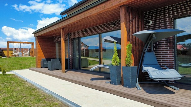Un edificio moderno con terraza de madera, asientos exteriores y amplios ventanales.