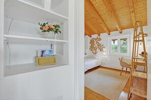 Un dormitorio con cama, escritorio, silla, escalera y ventana con vistas.