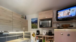 A modern kitchen with wooden cabinets, a microwave, a refrigerator, and a television displaying a news channel.