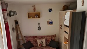 A cozy room with a patterned sofa, a small stool, a white chair, a fluffy rug, and a wooden ladder.