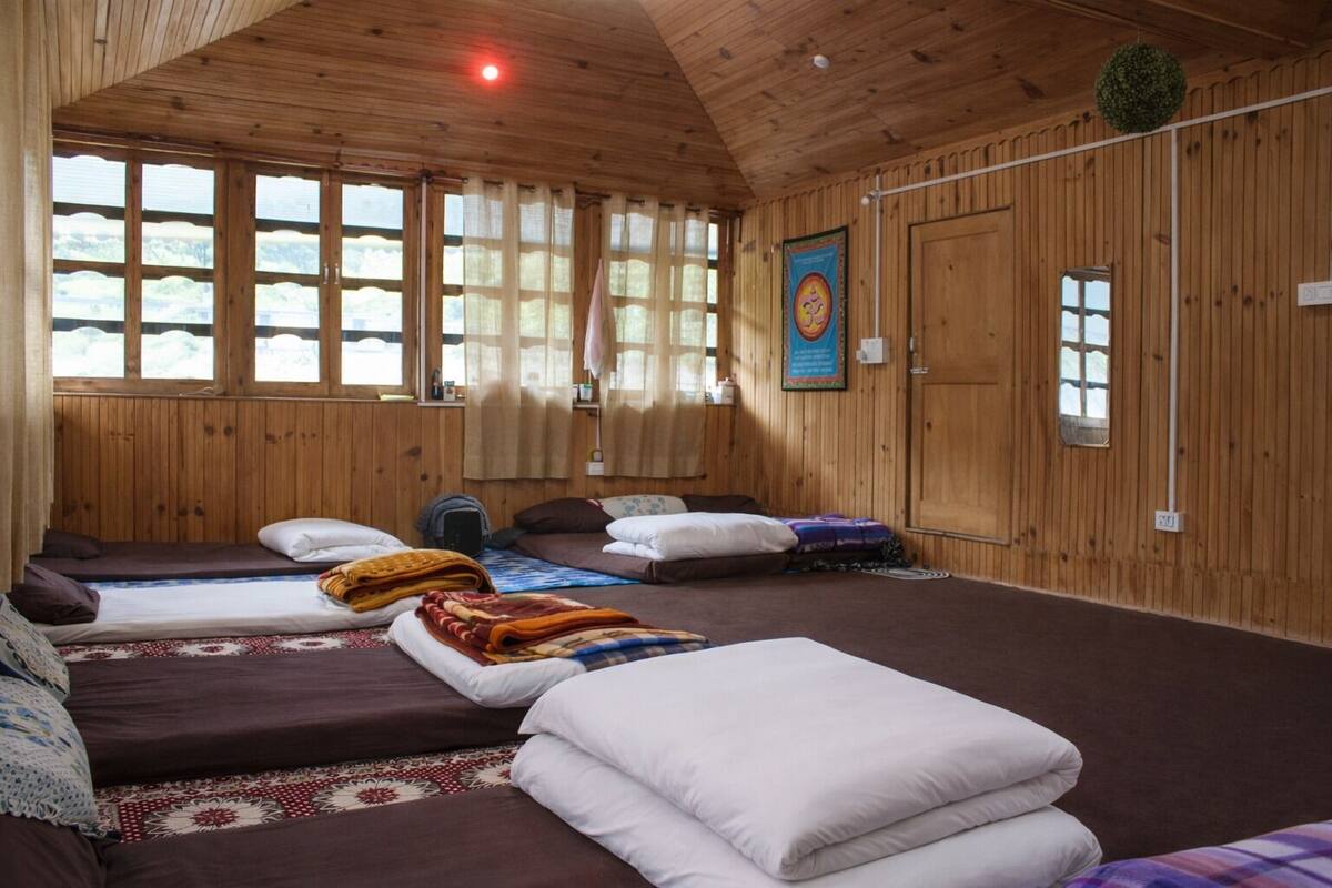 A room with wooden walls, multiple beds, a large window, and a door.