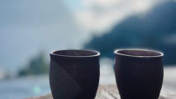 Dos tazas de cerámica sobre una superficie de madera, con un fondo desenfocado de montañas y cielo.