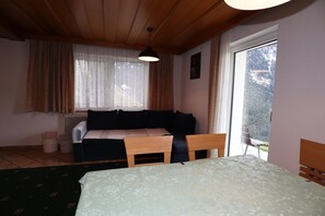 A room with a bed, a wooden table, a sofa, and a window with curtains. - Cozy Apartment With a Beautiful View (Kappl)