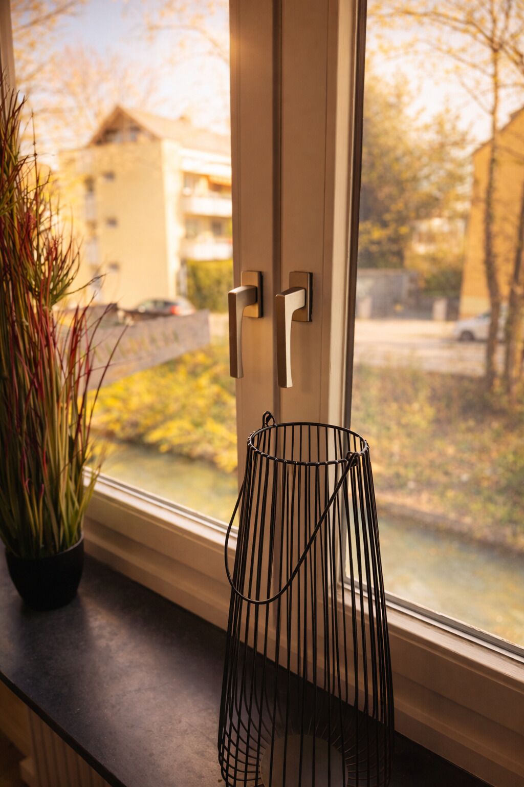 A window with a metal door handle and a black wire basket on the sill.